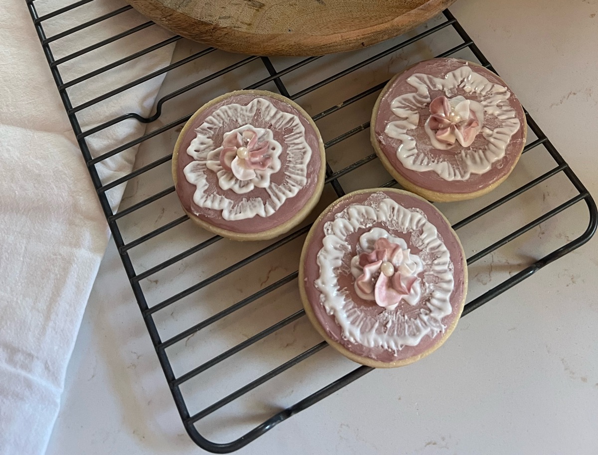 Round mauve sugar cookies with white piped ruffles and pink flowers
