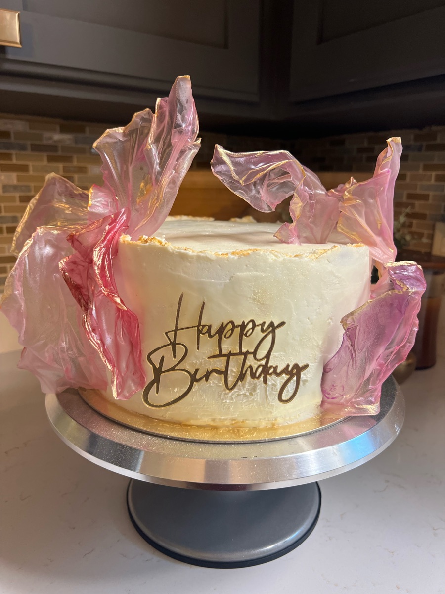 White buttercream birthday cake with sheer pink sails and a gold Happy Birthday topper